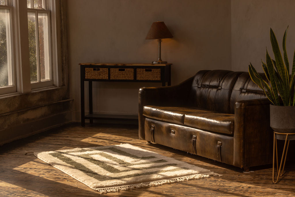 Light is peering through a vintage window, shining on a soft handwoven Moroccan rug.  This is a great interior design photo with a leather couch behind a soft plush rug. 